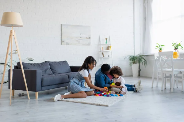 Afro-américaine mère et mamie jouer jeu de blocs de construction avec fille sur le sol dans le salon spacieux — Photo de stock