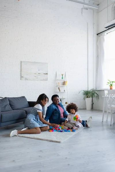 Toddler african american child playing with colorful building blocks near granny and mom on floor in living room — Stock Photo