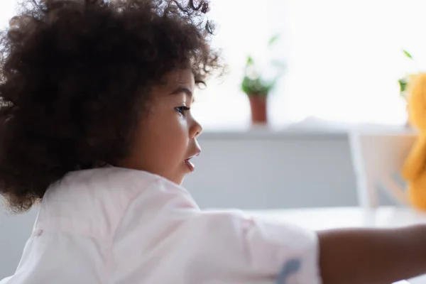 Vue latérale de la fille afro-américaine bouclée à la maison, premier plan flou — Photo de stock