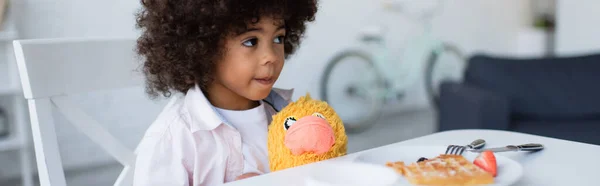 African american girl with soft toy sitting at table near waffle on plate, banner — Stock Photo