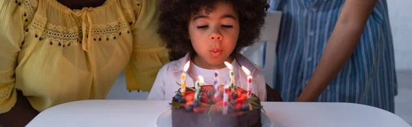 Ragazza afro-americana del bambino che soffia candele sulla torta di compleanno vicino a madre e nonna, striscione — Foto stock