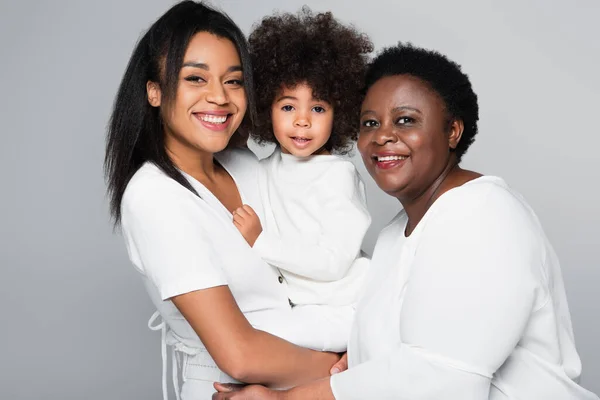 Afrikanische amerikanische Mädchen in den Händen von glücklichen Mutter und Oma Blick auf Kamera isoliert auf grau — Stockfoto