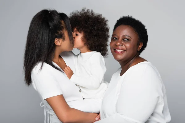 Jeune femme afro-américaine embrassant fille près de maman d'âge moyen souriant à la caméra isolée sur gris — Photo de stock