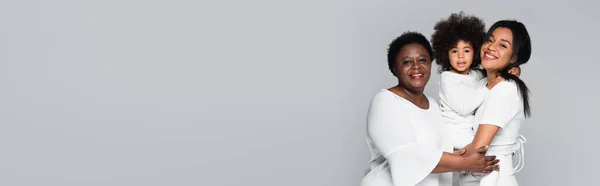 Young african american woman with mother and daughter smiling at camera isolated on grey, banner — Stock Photo