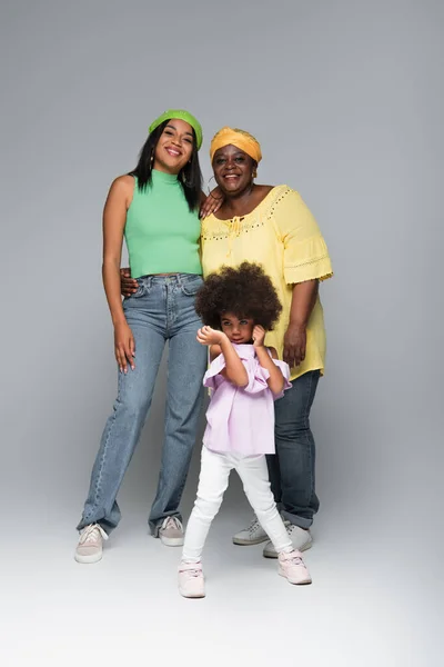 Happy and stylish african american women posing near toddler girl on grey — Stock Photo