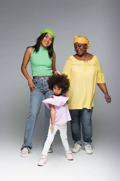 Heureuse femme afro-américaine posant avec maman et fille élégantes sur gris — Photo de stock