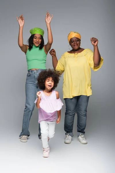 Cheerful african american women with girl in trendy clothes dancing on grey — Stock Photo