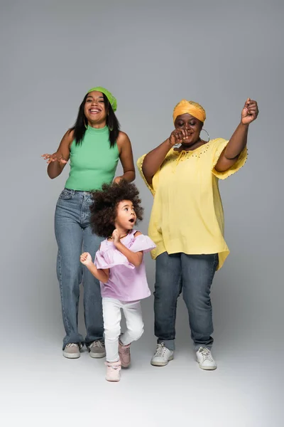 African american girl dancing with mother and granny in stylish clothes on grey — Stock Photo