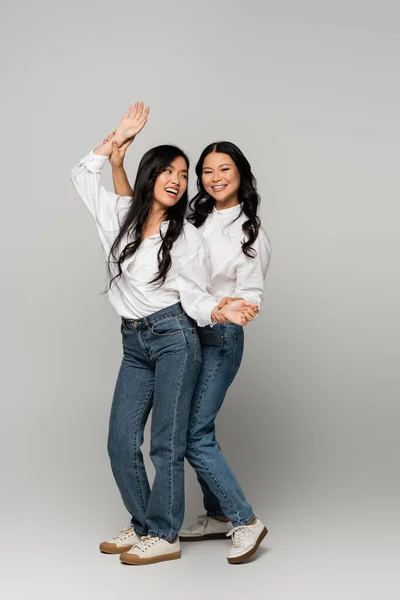 Full length of asian mother and excited daughter in blue jeans and white shirts on grey — Stock Photo