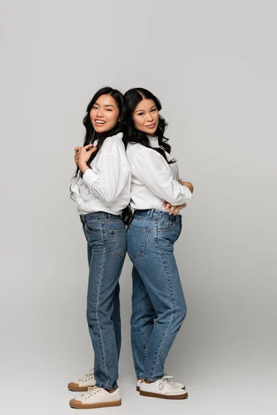 In voller Länge glückliche asiatische Mutter und Tochter in blauen Jeans und weißen Hemden auf grau — Stockfoto