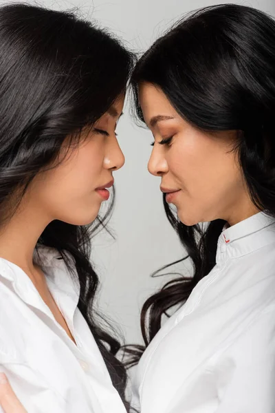 Vista lateral de madre asiática e hija en camisas blancas aisladas en gris - foto de stock