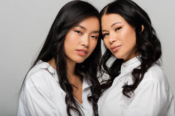 Азиатская мать и дочь в белых рубашках, смотрящих в камеру, изолированную на сером — стоковое фото