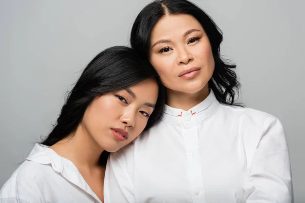 Asian young adult daughter leaning on shoulder of mother isolated on grey — Stock Photo