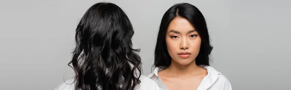 Back view of brunette asian mother near young adult daughter isolated on grey, banner — Stock Photo