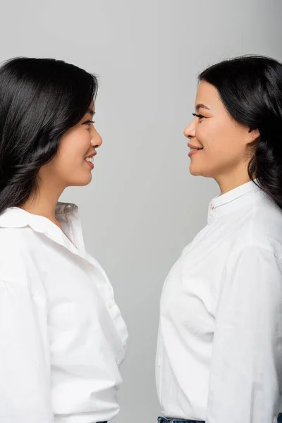 Side view of happy asian mother looking at cheerful young adult daughter isolated on grey — Stock Photo
