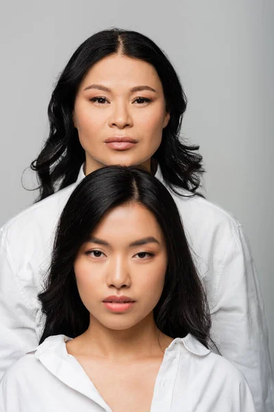 Morena asiático madre cerca joven adulto hija aislado en gris - foto de stock