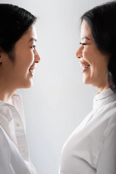 Side view of joyful asian mother looking at cheerful young adult daughter isolated on grey — Stock Photo