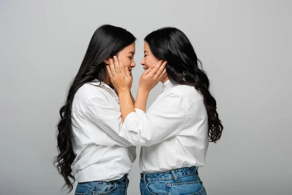 Side view of happy asian mother and young adult daughter touching cheeks of each other isolated on grey — Stock Photo