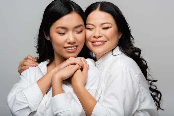 Fröhlich asiatische Mutter und junge erwachsene Tochter Umarmung isoliert auf grau — Stockfoto