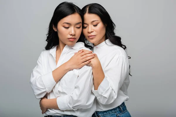 Брюнетка мати і азіатська молода дочка обіймає один одного і тримає руки ізольовані на сірому — стокове фото