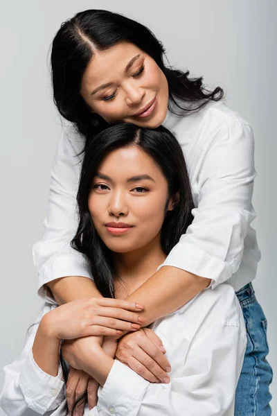 Любляча азіатська мати обіймає молоду дочку ізольовано на сірому — стокове фото