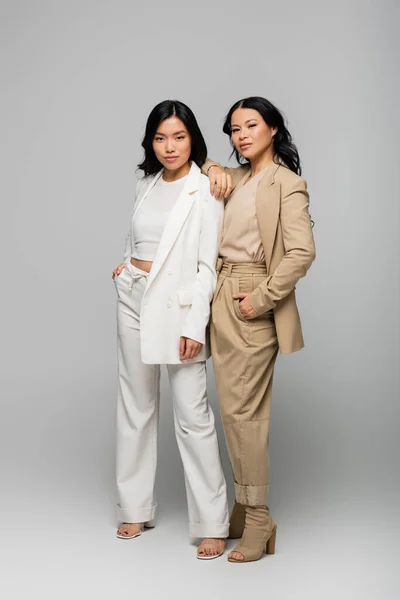 Longitud completa de moda asiático madre y joven adulto hija en trajes posando en gris - foto de stock