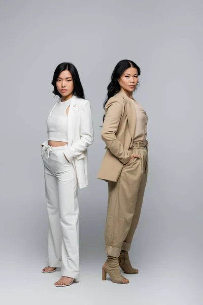 Full length of stylish asian mother and young adult daughter in suits posing on grey — Stock Photo