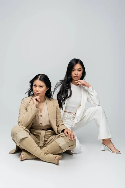 Piena lunghezza di elegante asiatica madre e bruna giovane figlia adulta seduta sul grigio — Foto stock