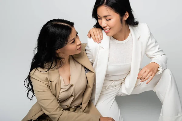 Стильная азиатская мать и счастливая молодая взрослая дочь смотрят друг на друга на сером — стоковое фото