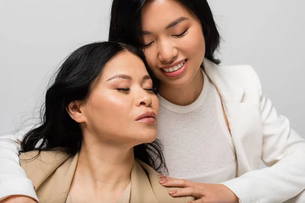 Happy asian young daughter hugging mother isolated on grey — Stock Photo