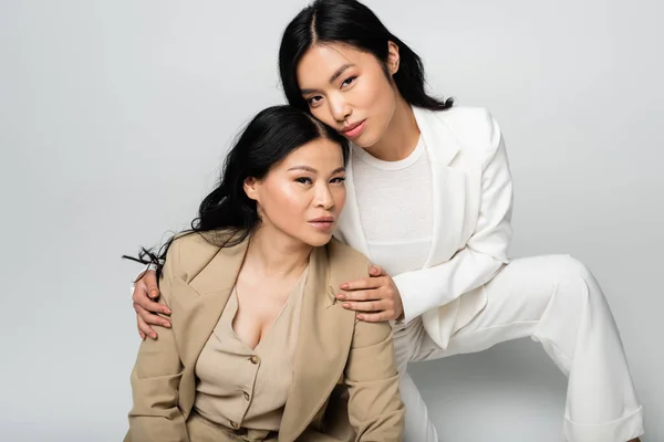 Asian young daughter hugging brunette mother on grey — Stock Photo