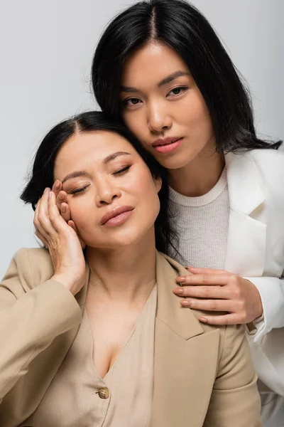 Asian young adult daughter hugging brunette mother isolated on grey — Stock Photo