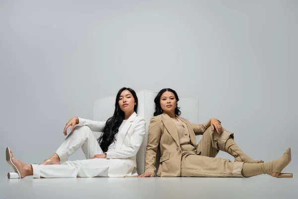 Comprimento total da moda asiática jovem mulher adulta sentada com mãe morena perto de cubo no cinza — Fotografia de Stock