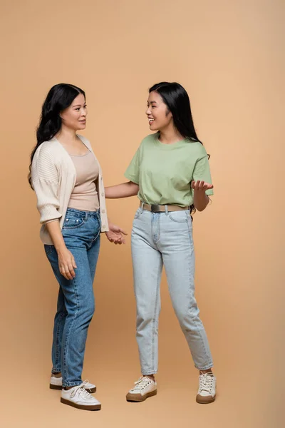 Full length of happy asian mother in jeans looking at daughter on beige — Stock Photo