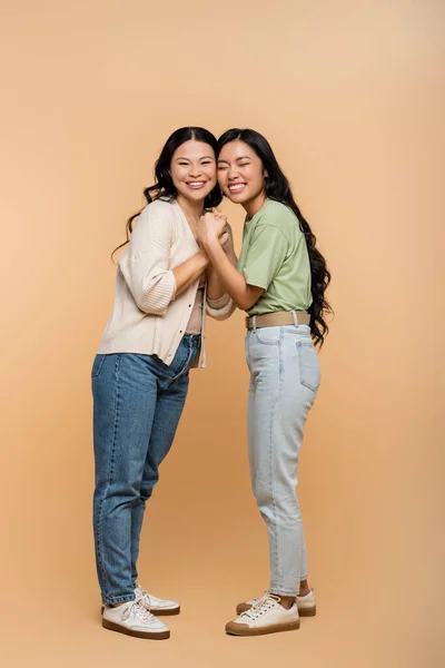 Full length of happy asian mother and daughter holding hands on beige — Stock Photo