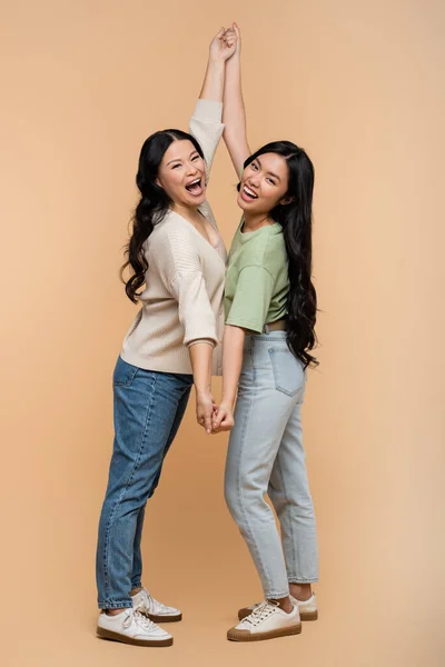 Comprimento total de espantado asiático mãe e filha segurando as mãos no bege — Fotografia de Stock