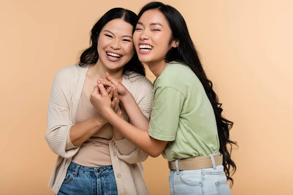 Cheerful asian mother and daughter holding hands isolated on beige — Stock Photo