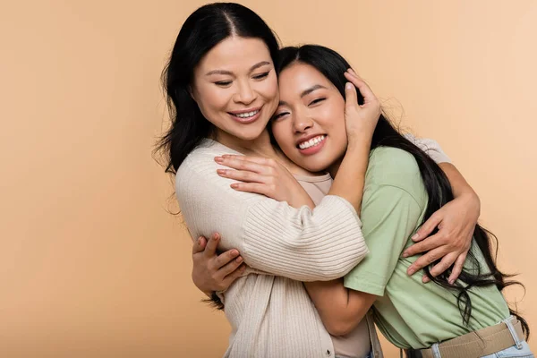 Cheerful asian mother and daughter hugging isolated on beige — Stock Photo