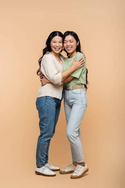 Volle Länge der fröhlich asiatische Mutter umarmt junge erwachsene Tochter auf beige — Stockfoto