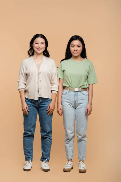 Full length of cheerful asian mother and adult daughter standing on beige — Stock Photo