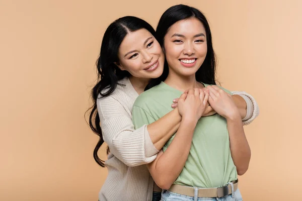 Brunette asian woman hugging adult daughter isolated on beige — Stock Photo