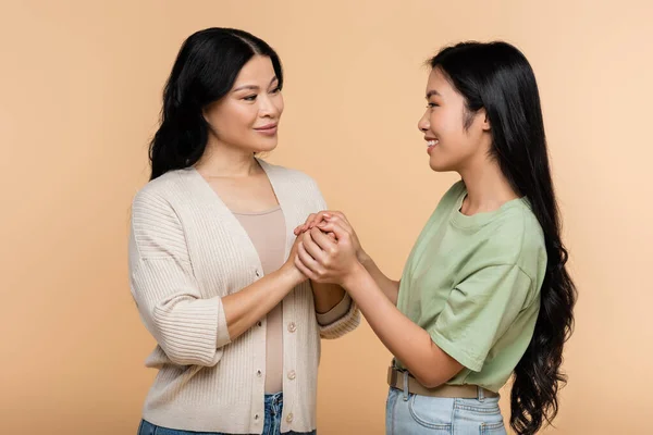 Felice donna asiatica che si tiene per mano con figlia adulta isolata sul beige — Foto stock