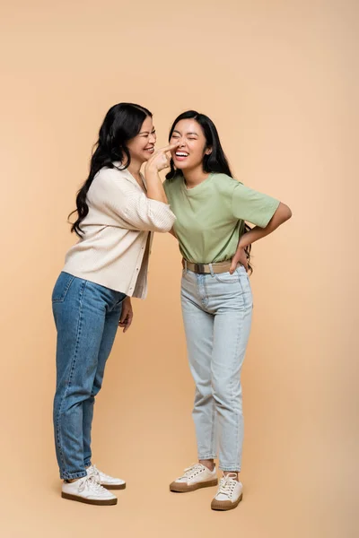 Full length of cheerful asian mother touching nose of pleased young adult daughter on beige — Stock Photo