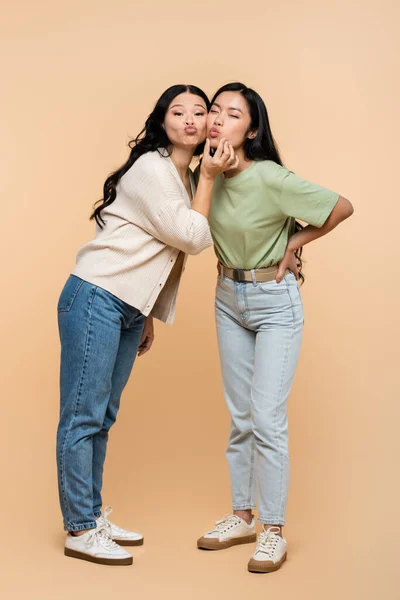 Full length of funny asian mother touching face of young adult daughter and pouting lips on beige — Stock Photo