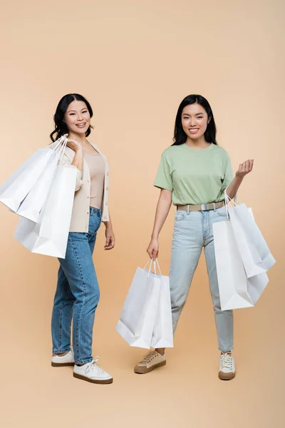 Longitud completa de feliz asiático madre y hija con bolsas de compras en beige - foto de stock