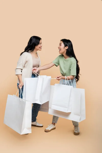 Volle Länge der fröhlichen asiatischen Mutter und Tochter mit Einkaufstaschen auf beige — Stockfoto