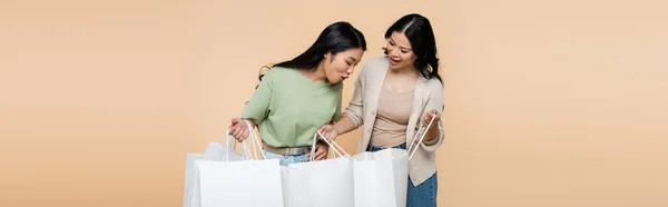 Sorpreso asiatico donna guardando shopping bag vicino madre isolato su beige, striscione — Foto stock