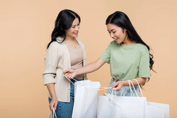 Glückliche asiatische Frau schaut auf Einkaufstasche nahe Mutter isoliert auf beige — Stockfoto