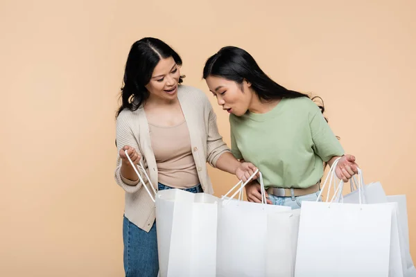 Überraschte Asiatin sieht Einkaufstasche nahe Mutter isoliert auf Beige — Stockfoto