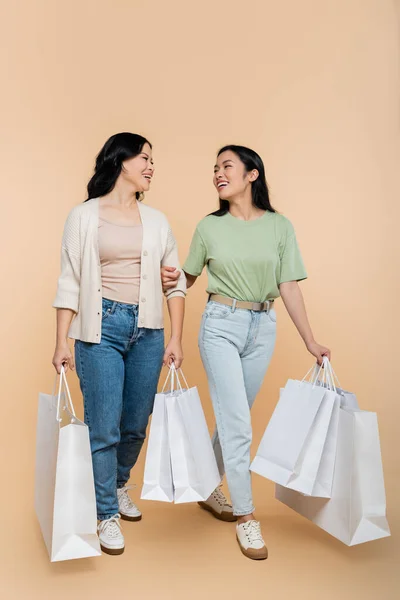 Volle Länge der asiatischen Mutter und glücklich junge erwachsene Tochter lächelt, während sie Einkaufstüten auf beige halten — Stockfoto